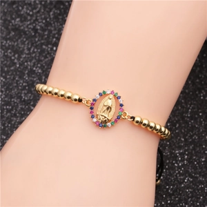 Detail of gold beaded bracelet with colorful zircon Virgin Mary medal on wrist