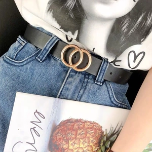 Fashionable women's thin black leather belt with gold double ring buckle on denim jeans