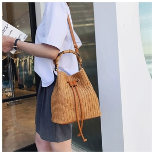 Detail of hand-woven straw bucket bag featuring bamboo handle and leather drawstring closure