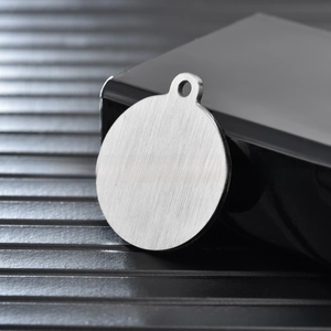 Close-up of brushed stainless steel round pet tag with pre-drilled hole for engraving