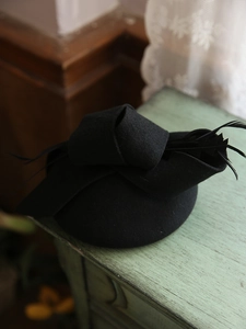 Elegante tocado vintage negro con lazo y detalle de plumas sobre mesa de madera rústica