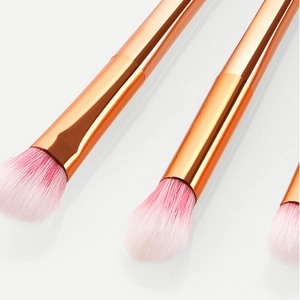 Rose gold eye shadow brush set with pink gradient bristles on a white reflective surface