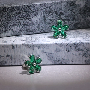 Macro view of flower-shaped stud earrings with green pear-cut stones and silver beads