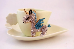 Detail of crystal encrusted unicorn keychain with blue wings on a decorative cup