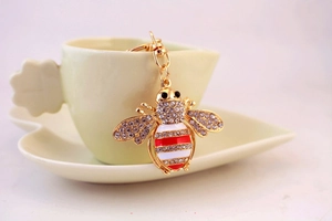 Close-up of crystal honey bee keychain with red stripes hanging on a ceramic cup