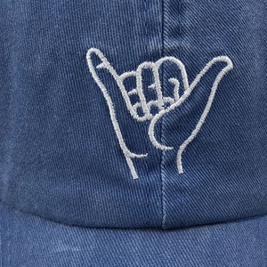 Macro shot of white shaka embroidery on dark blue washed cotton baseball cap