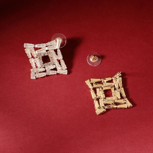 Detail of square gold earrings with hollow maze pattern and zircon inlay on red background