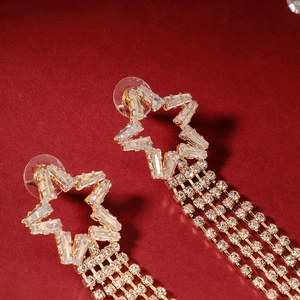 Detailed macro view of gold star tassel earrings with zircons on red velvet background