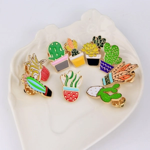 Detailed view of nine cactus enamel pins displayed on a white ceramic jewelry tray