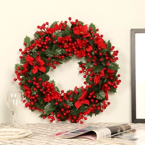 Christmas wreath with red poinsettias, berries, and green leaves on a beige wall