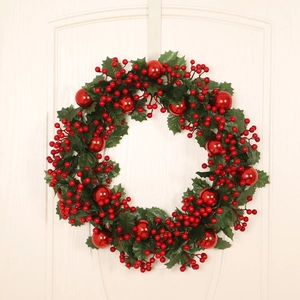 Christmas wreath with artificial green leaves, red berries and shiny baubles on a white door