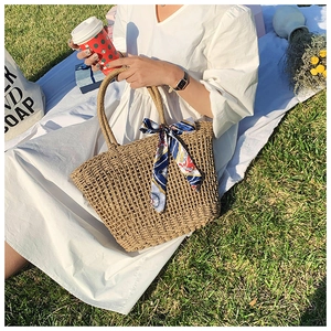 Straw tote bag with colorful silk scarf handle on picnic mat for summer beach