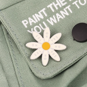 Close-up of daisy enamel pin with Yes and No petals on green canvas fabric texture