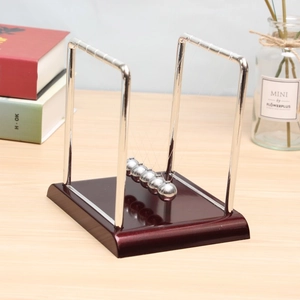 Newton's cradle with metal balls on wooden base set on a desktop with books and vase