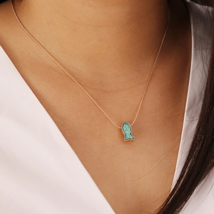 Close-up of a blue fish pendant with gold-plated chain worn by a fashion model