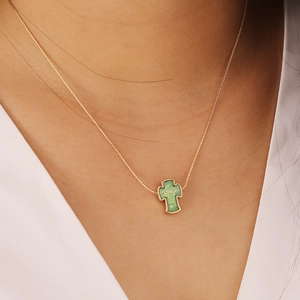Close-up of gold chain necklace featuring a green opal cross pendant on a model