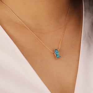 Close-up of a delicate gold necklace with a blue opal fish pendant on a female model