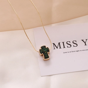 Detailed close-up of a golden cross necklace with a sparkling dark green opal inlay