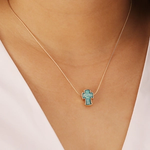 Detail view of a gold-plated cross necklace with a blue opal stone pendant on a model
