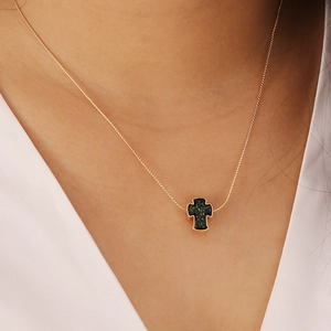 Detail of a gold cross necklace with shimmering dark green inlay worn by a model