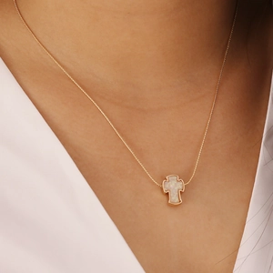 Detail of a gold cross necklace with a white opal pendant worn by a model