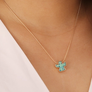 Close-up of a model wearing a gold angel necklace with a vibrant blue opal pendant