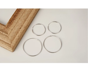 Macro shot of silver sterling hoop earrings in four different sizes on a beige backdrop