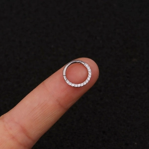 Macro view of a silver stainless steel nose ring with tiny zircons held on a fingertip