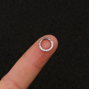 Close-up of a silver stainless steel hinged ring with tiny clear zircon stones on fingers