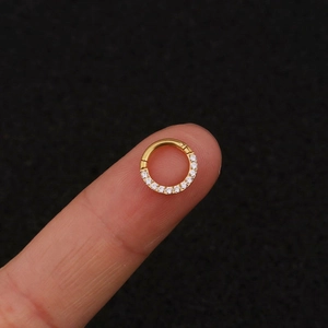 Macro shot of a gold stainless steel nose ring with zircon held on a fingertip