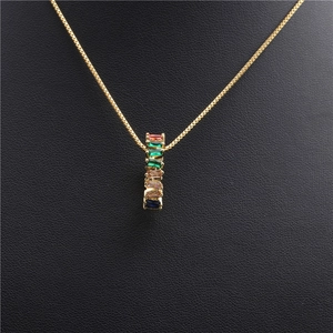 Detail of gold box chain necklace with cylinder pendant featuring colorful cubic zirconia stones