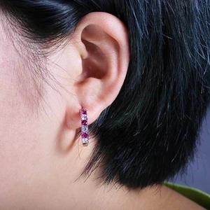 Close-up of silver hoop earring with pink and white zircon stones worn on the ear