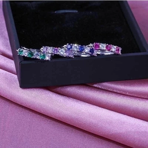 Detail view of four silver bands with colorful cubic zirconia on purple silk background