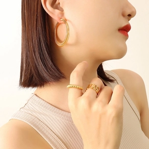 Professional model wearing large gold textured hoop earrings and minimal gold stacking rings