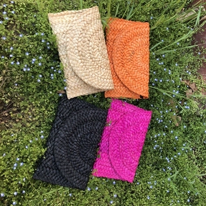 Pochette in paglia di mais intrecciata in beige, arancione, nero e rosa su erba verde