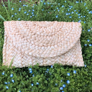 Pochette a busta in paglia di mais naturale su erba verde con piccoli fiori blu decorativi