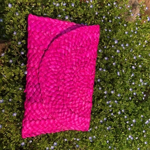 Pochette a busta in paglia intrecciata a mano fucsia su erba verde per un look estivo