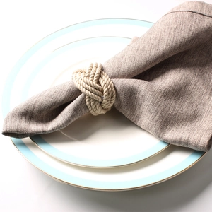 Close-up of handmade natural jute rope napkin ring on a beige linen napkin and ceramic plate