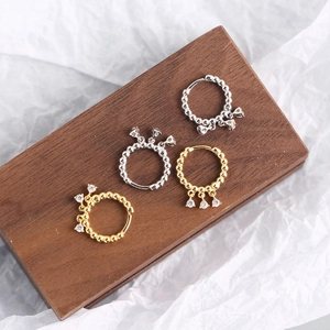 Detail of silver and gold zircon tassel earrings on dark wood with beaded textures