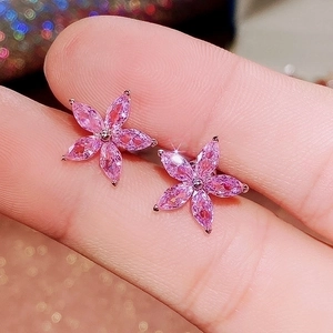 Macro shot of pink floral stud earrings with marquise-cut zircons held by fingers