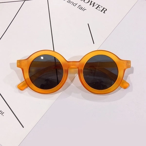 Detail view of round orange kids' sunglasses with matte frames and dark UV lenses