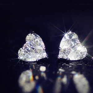 Sparkling heart-shaped stud earrings with clear zircon stones on a black reflective surface