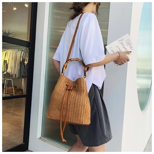 Close-up of vintage straw bucket bag featuring carbonized bamboo handle and leather drawstring