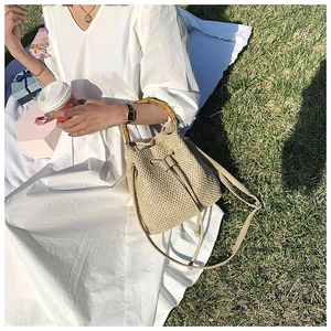 Detail of woven straw bucket bag with bamboo handle and leather drawstring on green grass