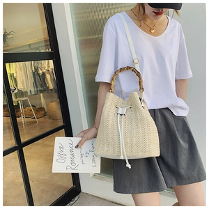 Detail of straw bucket bag with bamboo handle and white leather strap worn by model