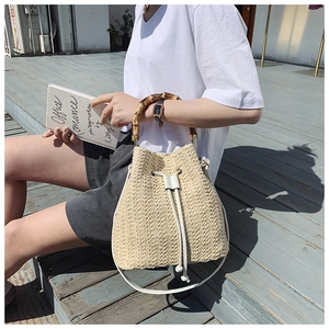 Detail of straw bucket bag with bamboo handle and drawstring closure in outdoor setting