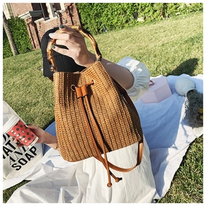 Detail of straw bucket bag featuring bamboo handle and leather drawstring closure