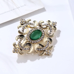 Dettaglio di spilla vintage dorata con gemma color smeraldo e cristalli luccicanti