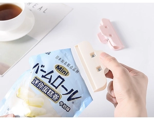 Close-up of a beige plastic food clip sealing a blue snack bag on a white table