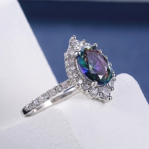 Detailed macro view of an oval mystic topaz ring with four-prong setting and pavé crystals